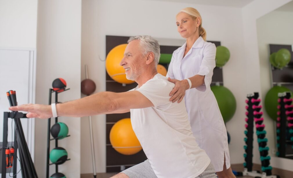 Mulher ajudando idoso com exercícios fisioterapêuticos