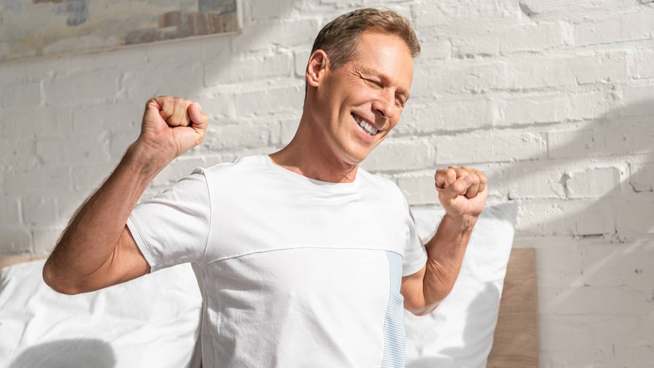 Homem levantando da cama feliz após alongamento matinal