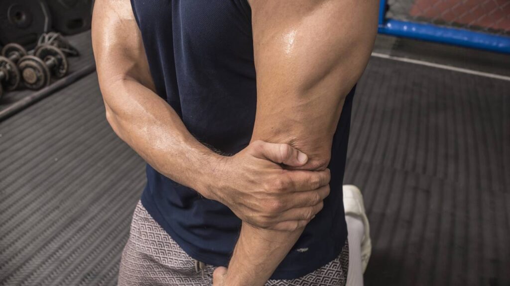 Homem segurando o próprio braço com dores em academia