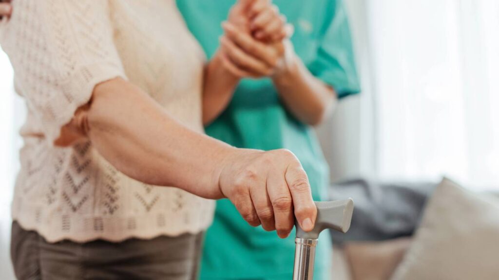 Senhora de idade com bengala sendo ajudada durante reabilitação pediátrica