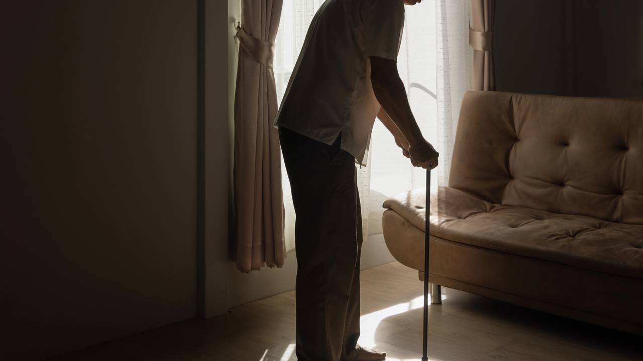 Idoso de pé em casa na sala com bengala
