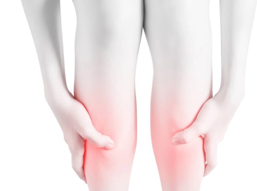 Mulher levando as mãos até as pernas sinalizando dor nas canelas