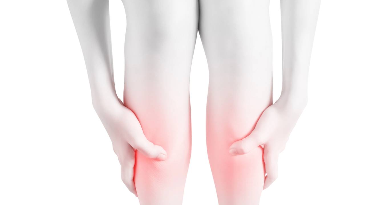 Mulher levando as mãos até as pernas sinalizando dor nas canelas